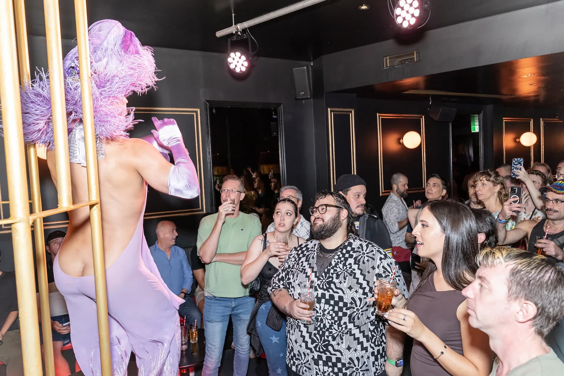 A drag performer inside the gold cage in The Caged Cocktail Bar as guests watch.