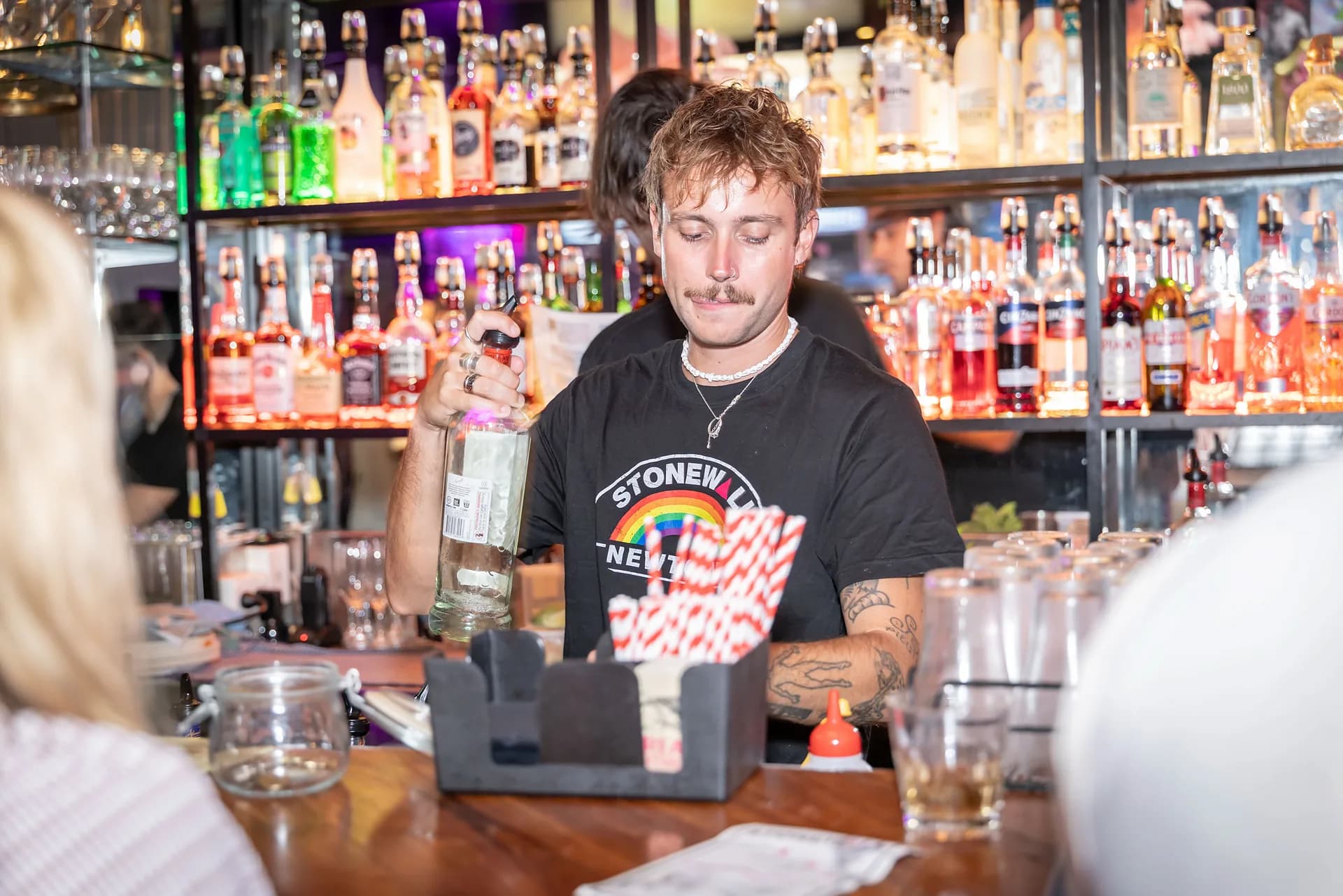 A bartender preparing drinks in front of Stonewall Newtown's illuminated back bar.