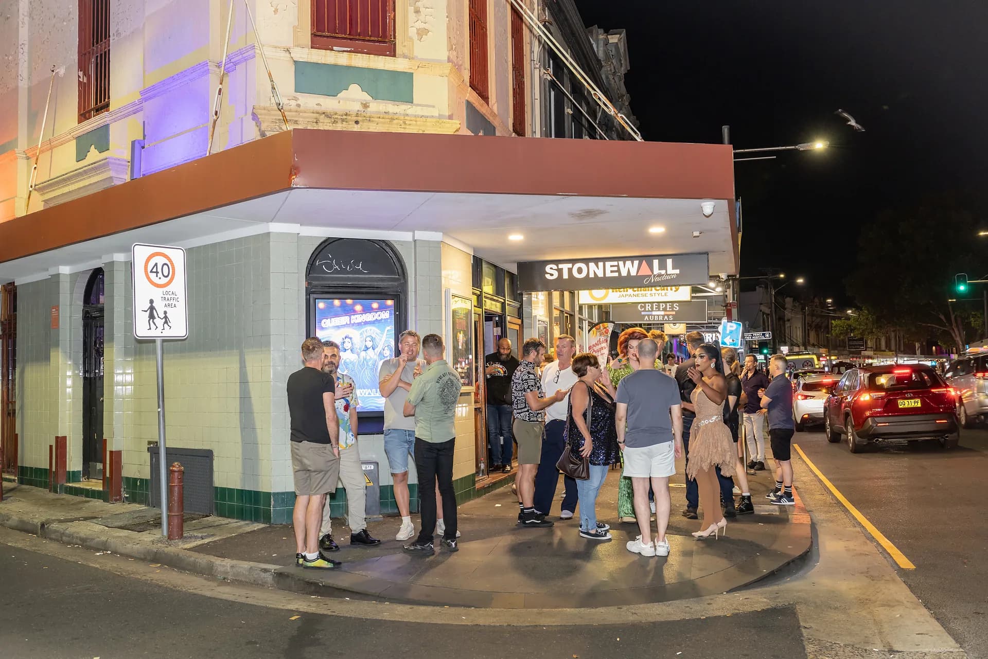 Guests gathering outside the illuminated Stonewall Newtown sign at night.